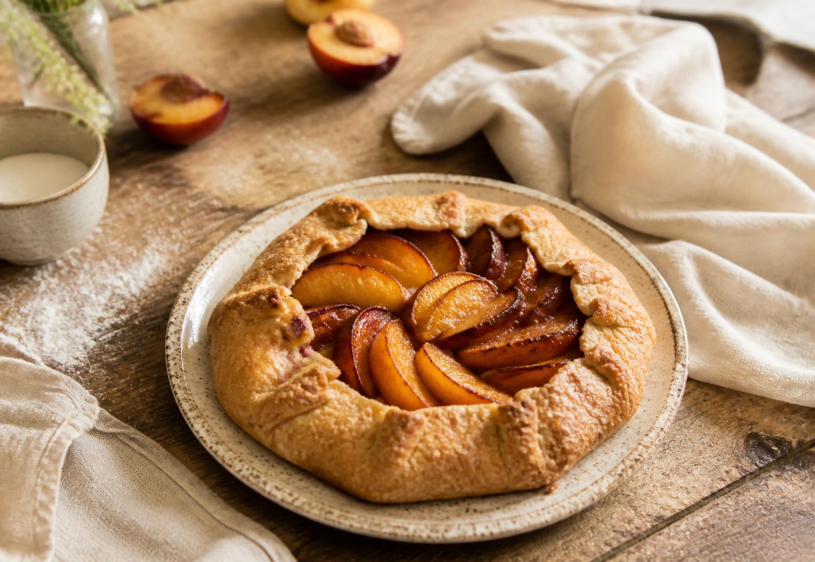 A stone fruit galette cooling on a ceramic plate on a wooden bakery table